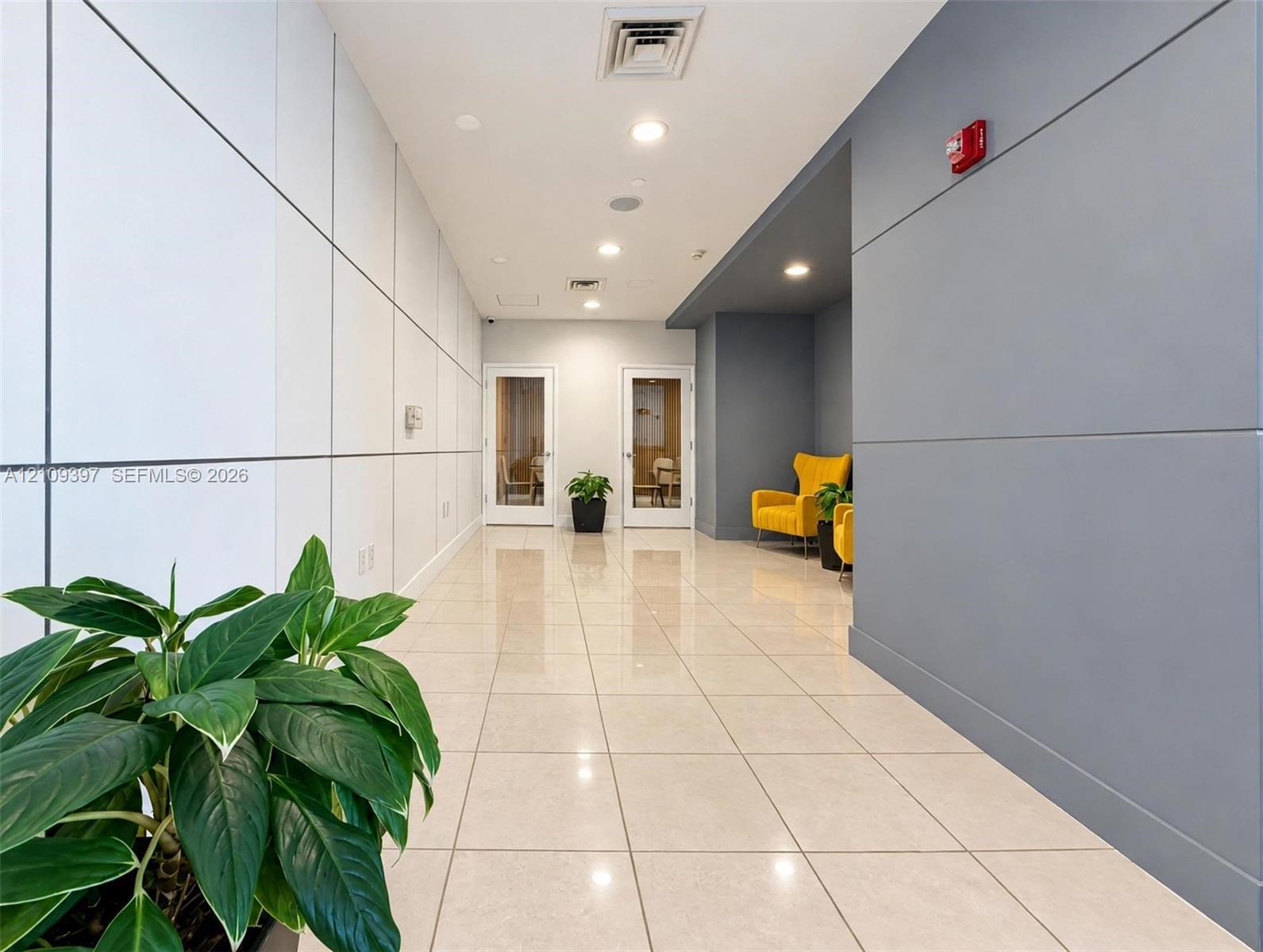 Contemporary corridor featuring large-format light tile flooring, white panel wall detailing, recessed ceiling lighting, and a contrasting charcoal-colored accent wall