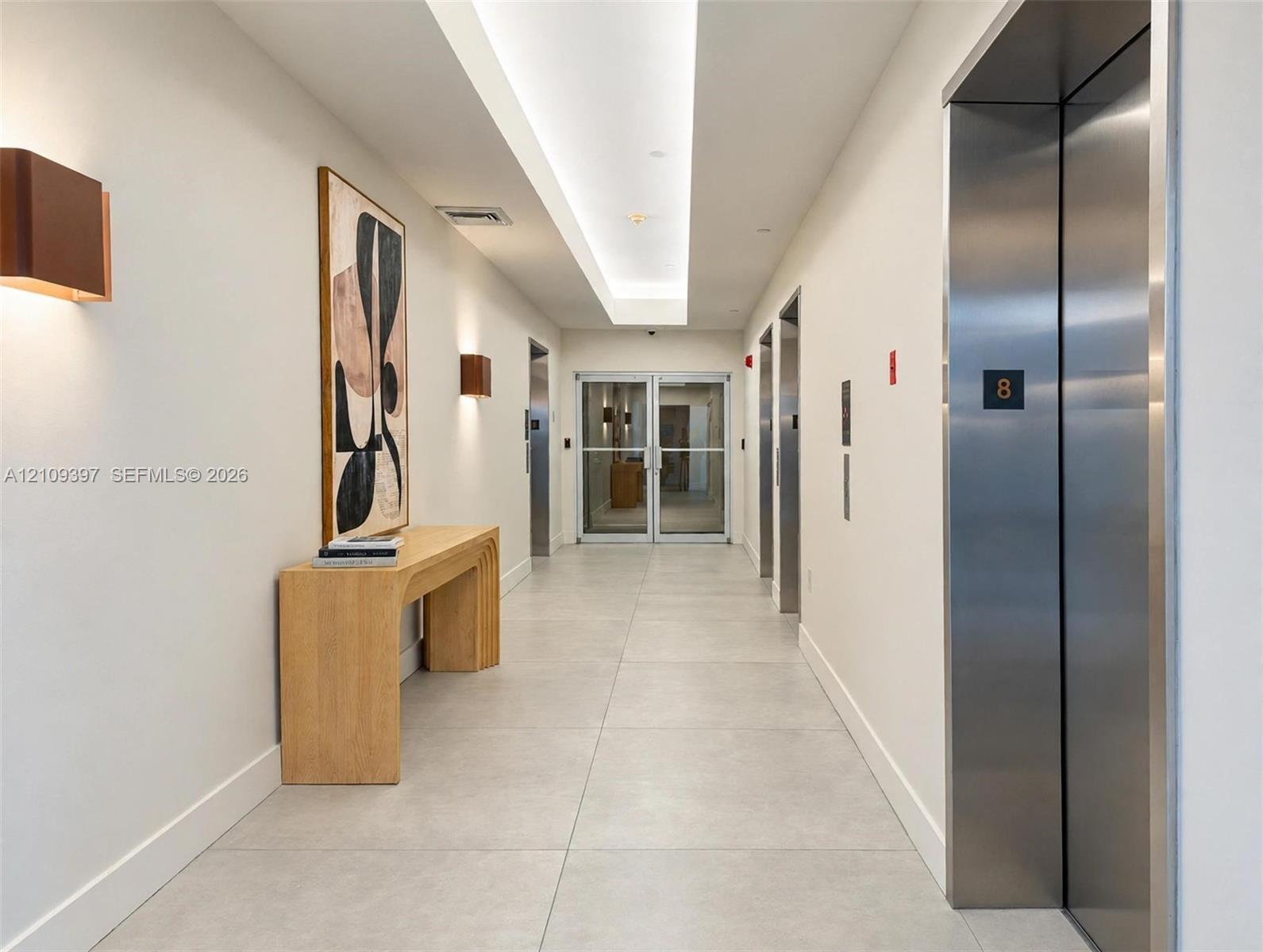 Hallway featuring stainless steel elevator doors, large-format tile flooring, recessed cove lighting, and wall-mounted sconce fixtures