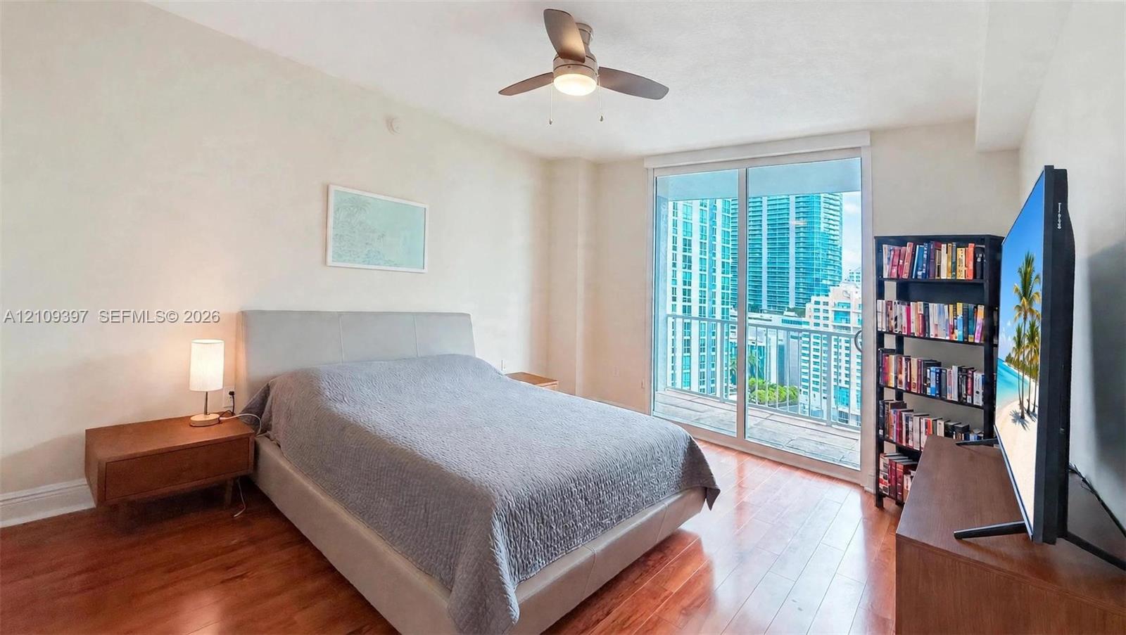 Wood-finish flooring, ceiling fan with integrated lighting, and floor-to-ceiling glass sliding doors opening to a private balcony