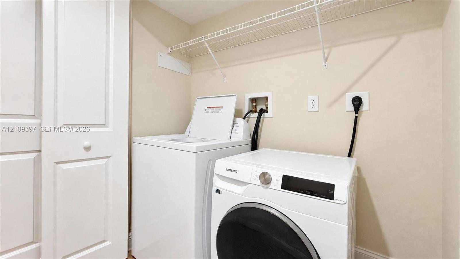Laundry area featuring built-in shelving, white paneled door, and recessed utility hookups