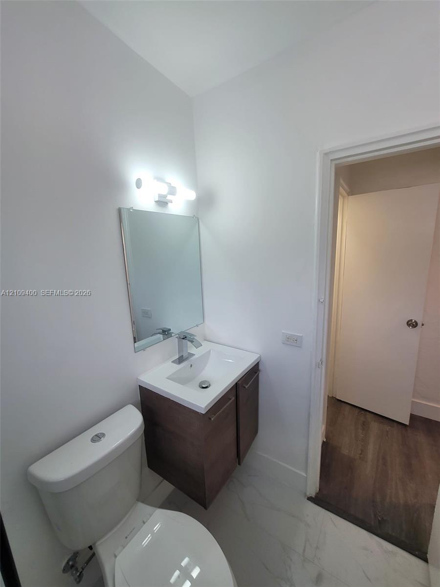 Floating vanity with wood-finish cabinetry, rectangular basin, chrome single-lever faucet, wall-mounted light fixture, and stone-finish tile flooring
