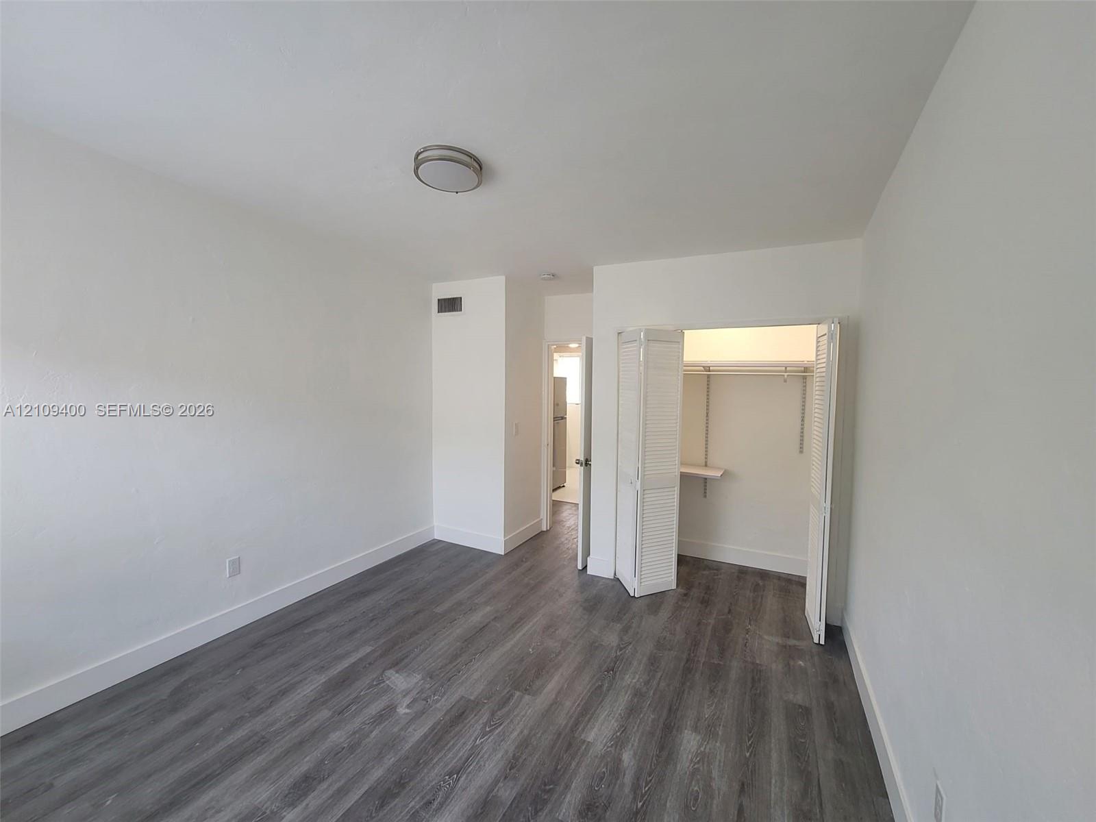 Room featuring wood-finish flooring, white walls, flush-mount ceiling lighting, and a closet with bifold louvered doors
