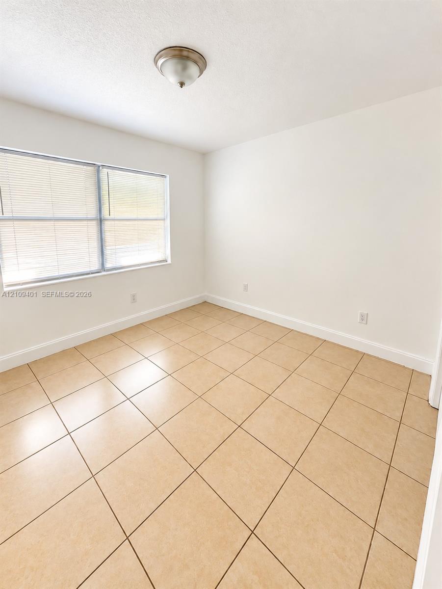 Neutral-toned ceramic tile flooring, crisp white wall finishes, and a flush-mount ceiling light fixture with an integrated window featuring horizontal blinds