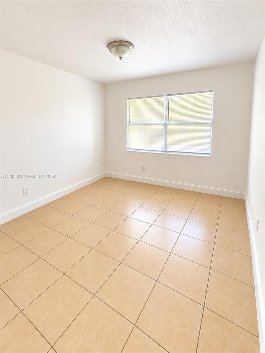 Room featuring neutral-toned tile flooring, large double-pane window with integrated blinds, and flush-mount ceiling lighting