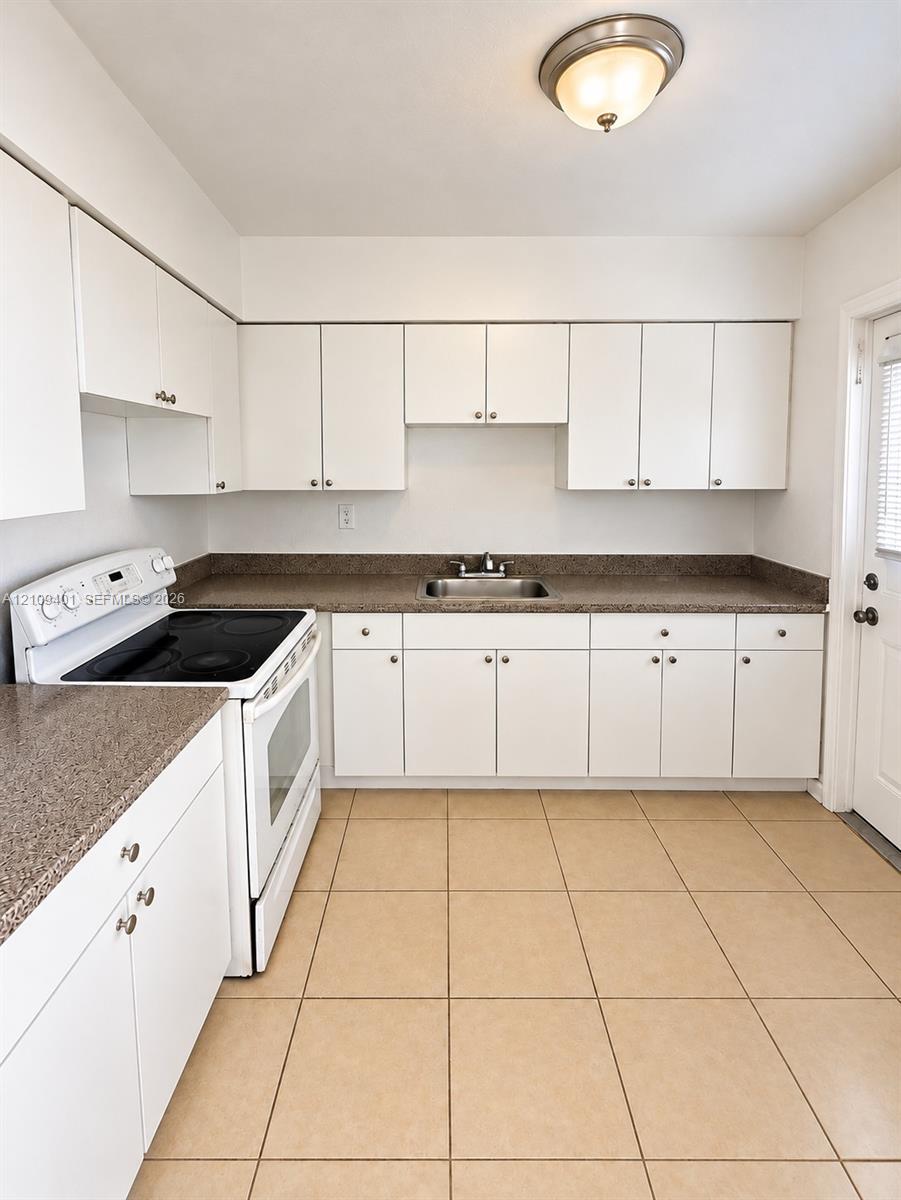 Kitchen featuring white shaker-style cabinetry, speckled stone-finish countertops, stainless steel sink with dual-handle faucet, ceramic tile flooring, and flush-mount ceiling lighting