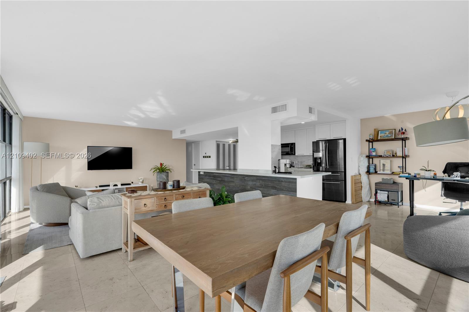 Open-concept interior featuring large-format tile flooring, a kitchen island with stone-surface countertops, and built-in white cabinetry