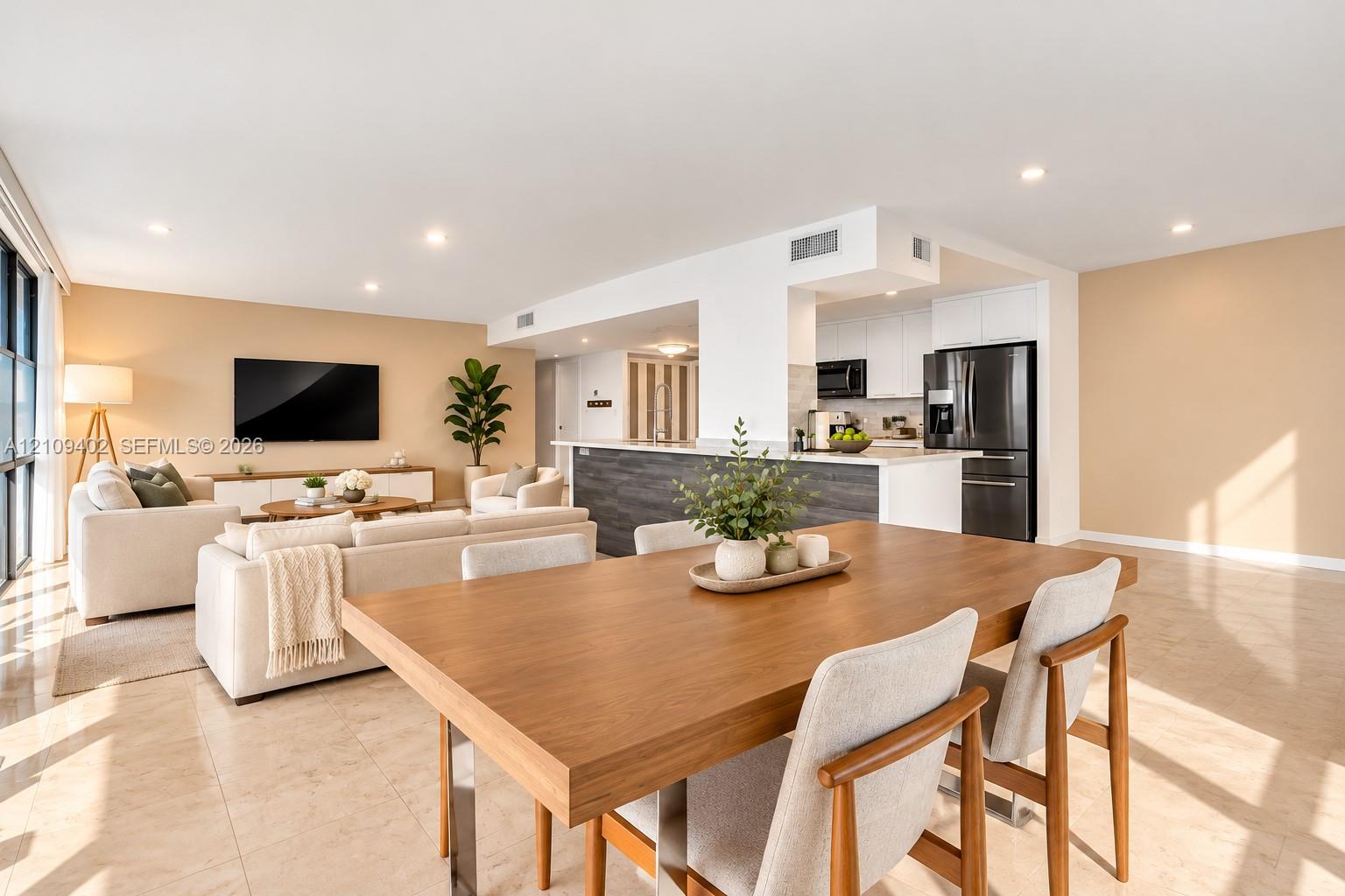 Open-concept interior featuring light-toned tile flooring, recessed ceiling lighting, and a kitchen island with dark-toned cabinetry and a white countertop