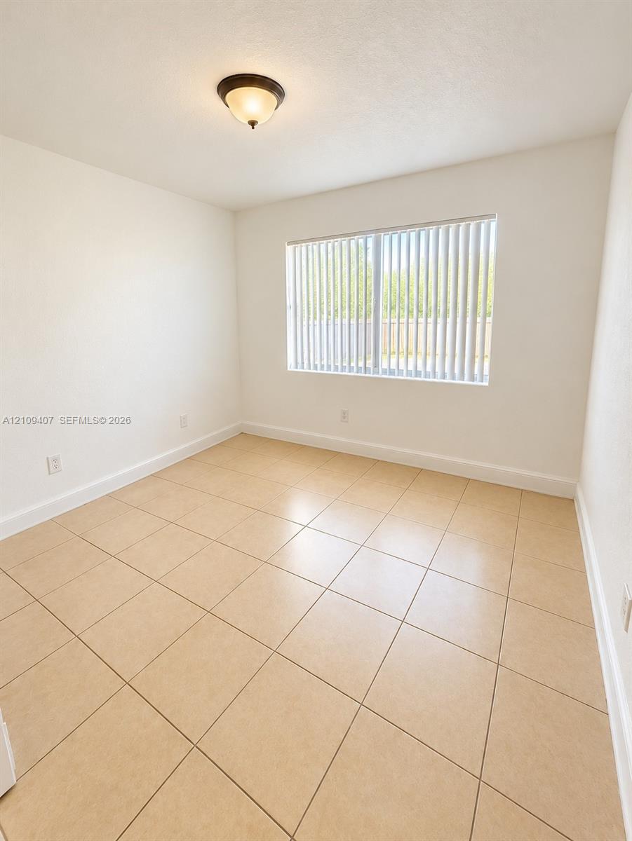 Room featuring neutral-toned tile flooring, light-colored walls, a single window with vertical blinds, and a dome-style flush-mount light fixture