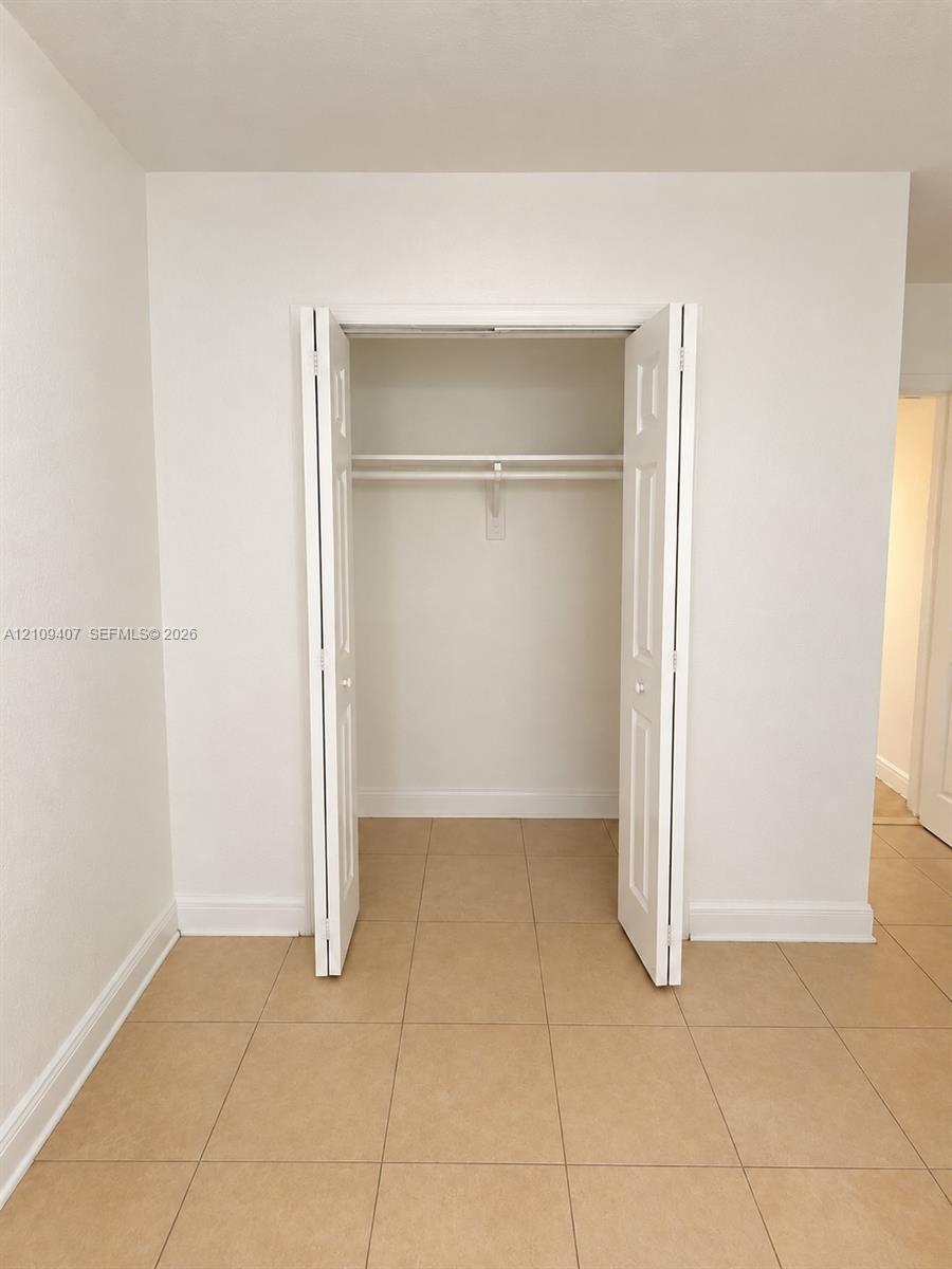 Interior space featuring neutral-toned tile flooring and a built-in closet with white six-panel bifold doors, an interior shelf, and a hanging rod