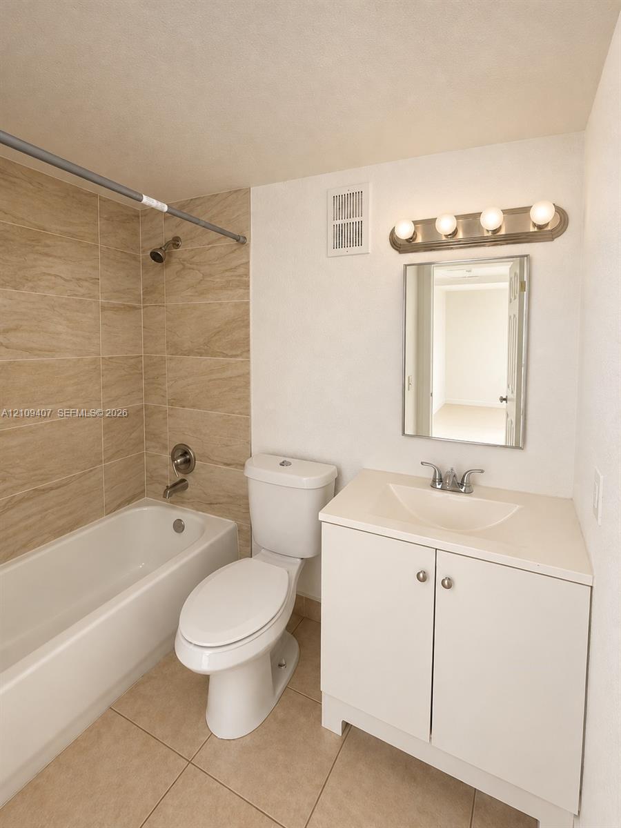 Bathroom featuring a white vanity cabinet with an integrated sink, neutral stone-finish floor tiling, and a shower-tub combination finished with textured wall tile