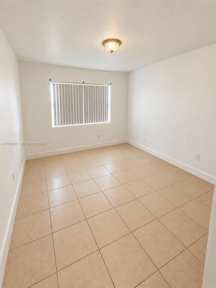 Neutral-toned tile flooring, white wall finishes, and a flush-mount ceiling light fixture, featuring a window with integrated vertical blinds