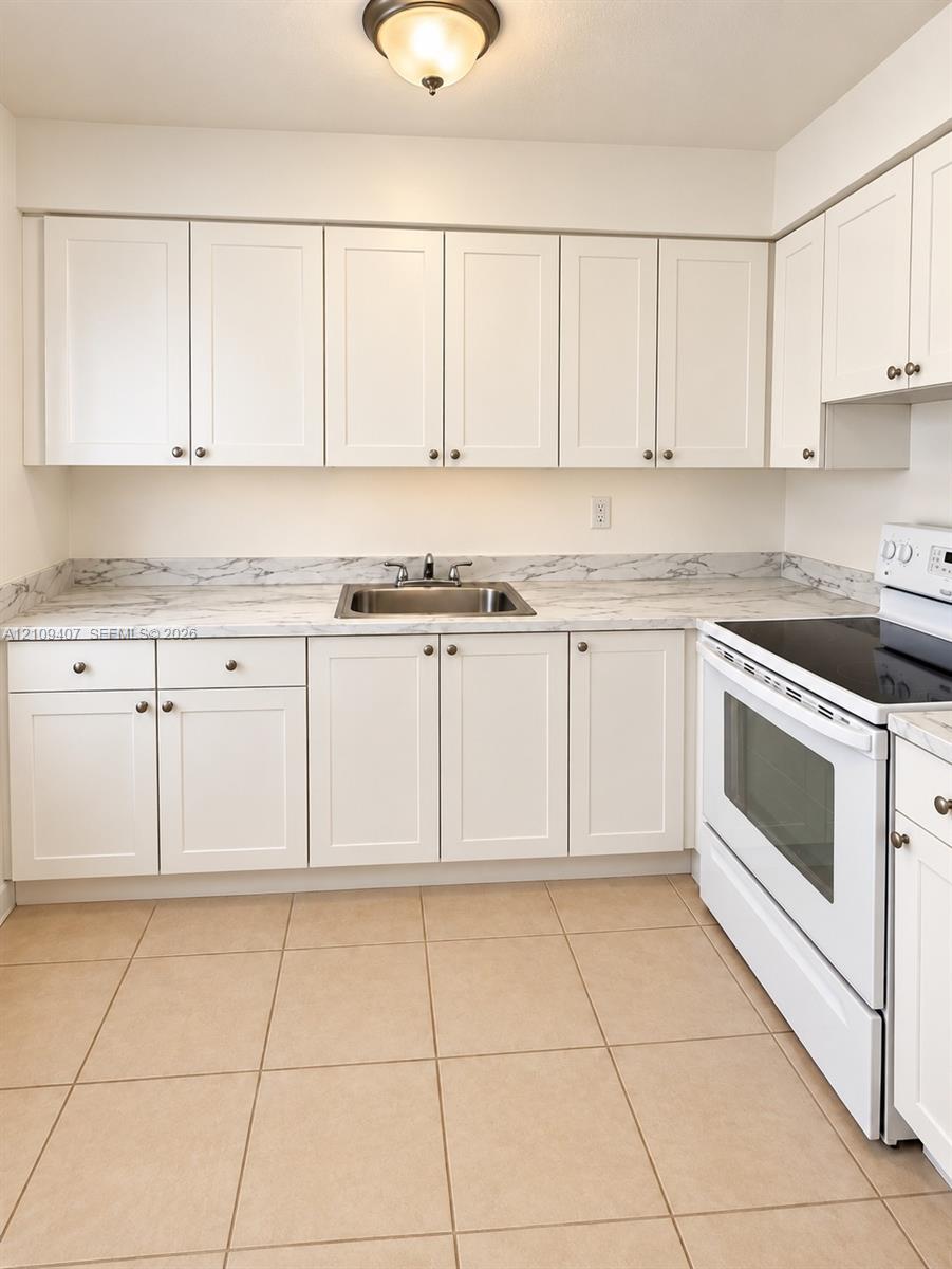 Kitchen featuring white shaker-style cabinetry, stone-pattern laminate countertops, a stainless steel sink with a dual-handle faucet, white electric range, and ceramic tile flooring