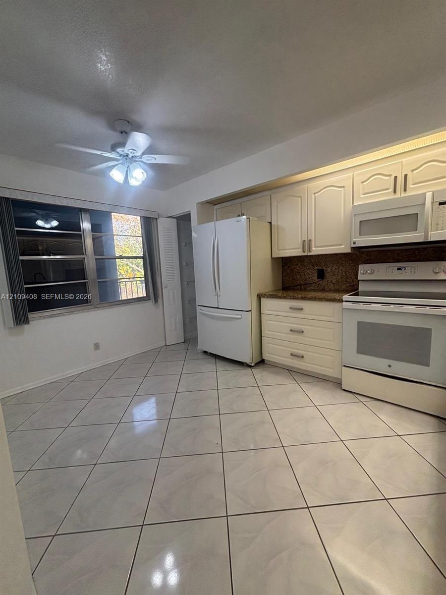 Kitchen featuring white cabinetry, stone-finish countertops, tiled flooring, built-in microwave, and ceiling fan with integrated lighting