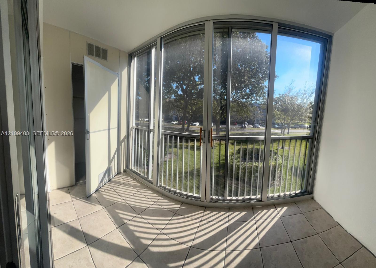 Enclosed balcony featuring tile flooring, a curved wall of floor-to-ceiling windows, and vertical metal railings