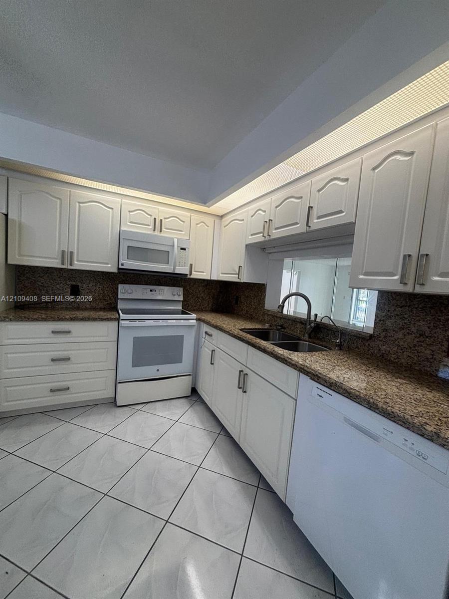 Kitchen featuring white cabinetry, stone-finish countertops, tile flooring, integrated over-range microwave, and a dual-basin sink with a gooseneck faucet