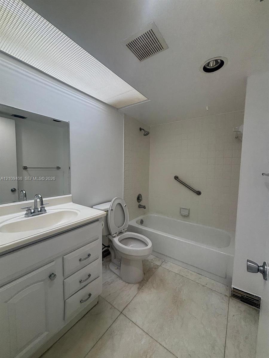 Bathroom featuring a skylight, vanity with an integrated sink and chrome faucet, tile flooring, and a bathtub with a tile surround