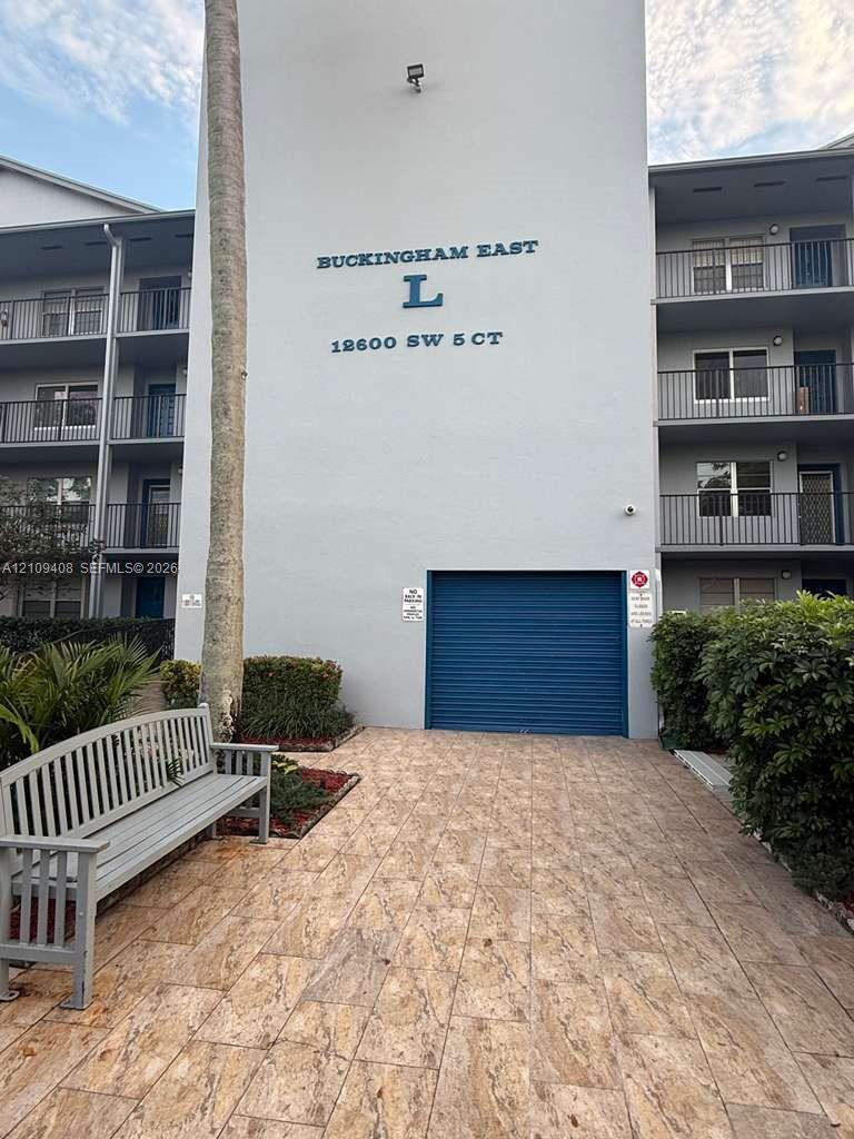 Multi-story exterior building facade with tile-patterned hardscaping, roll-down garage door, and private balconies featuring metal railings