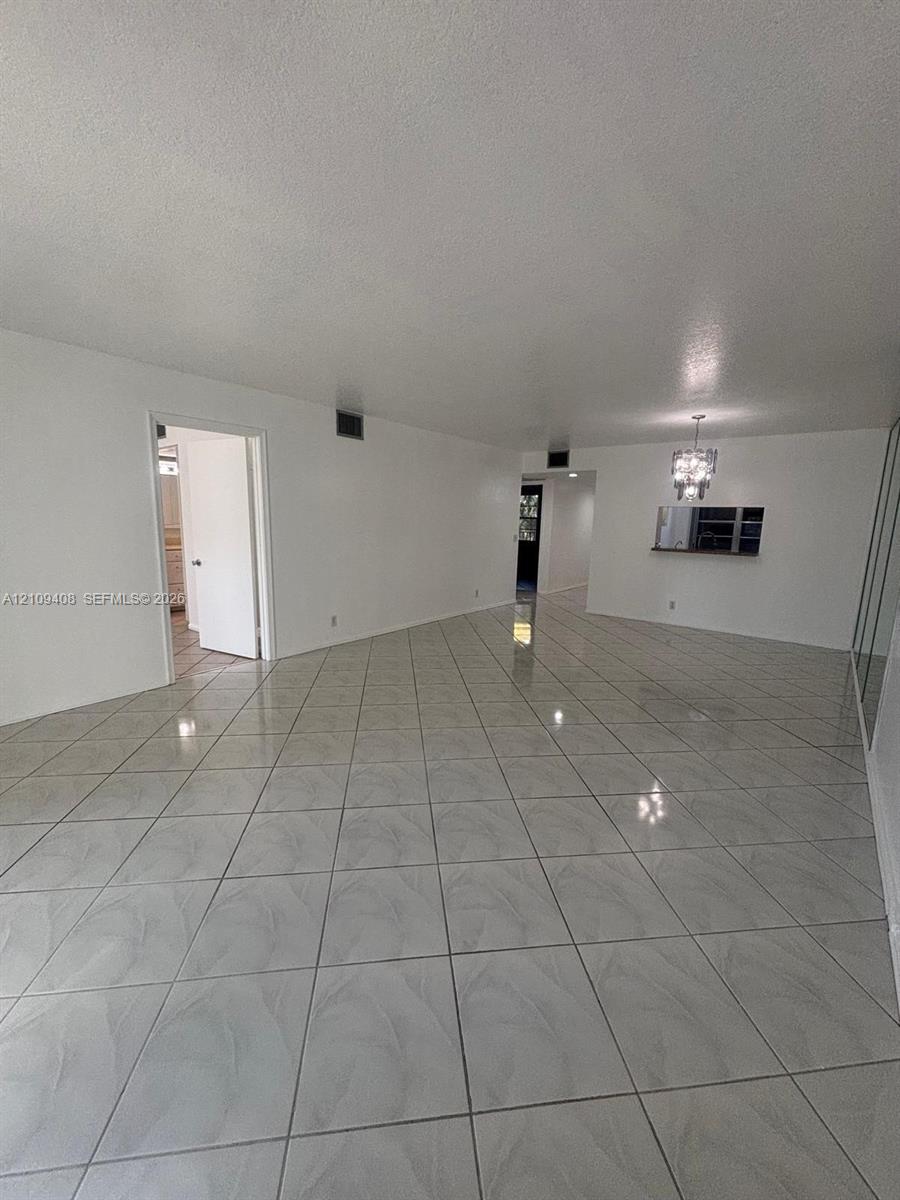 Spacious interior featuring large-format tile flooring, a built-in pass-through window with an attached pendant light fixture, and mirrored wall accents