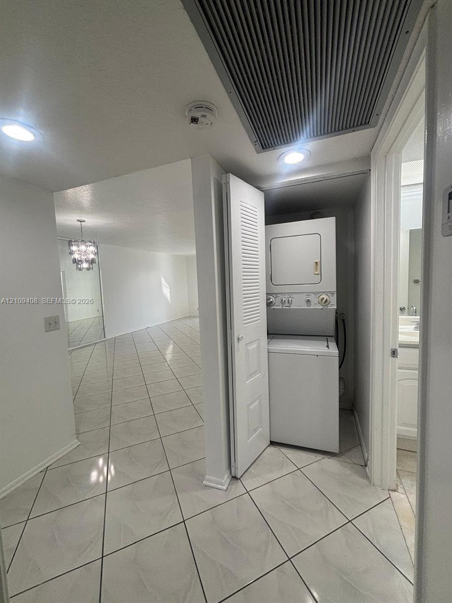Laundry area featuring a stacked washer and dryer unit enclosed by louvered bi-fold doors, complemented by ceramic tile flooring and recessed lighting