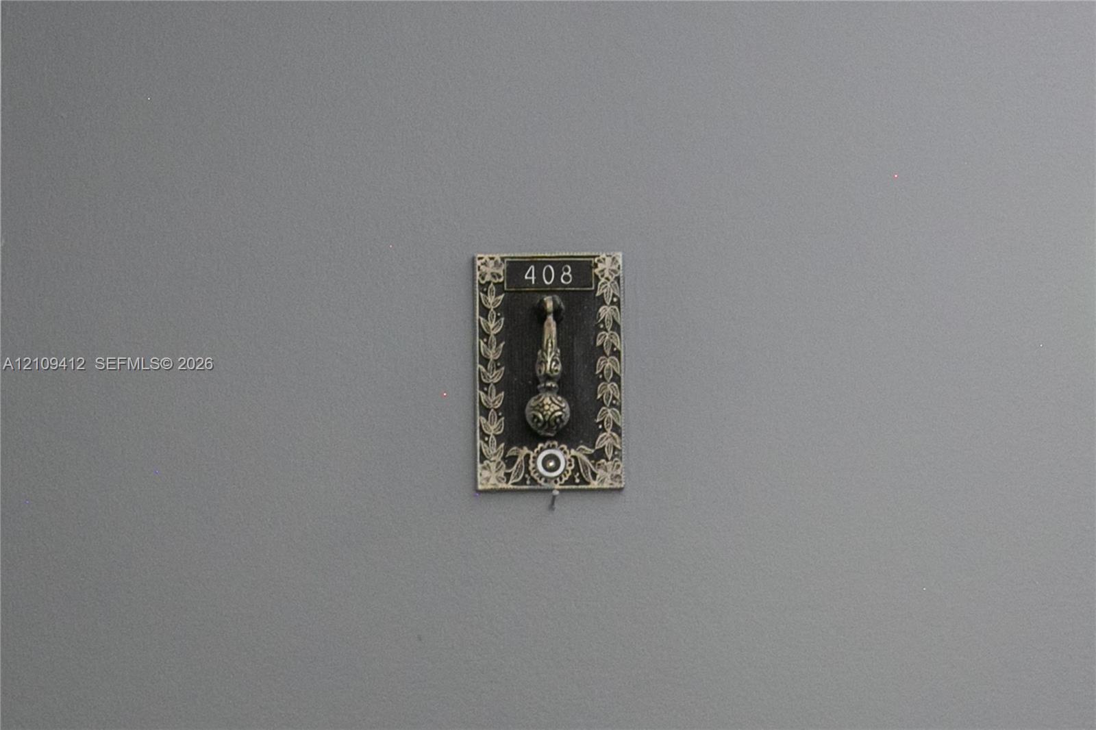 Decorative metal door knocker featuring an ornate floral border, engraved numbering, and a circular accent detail