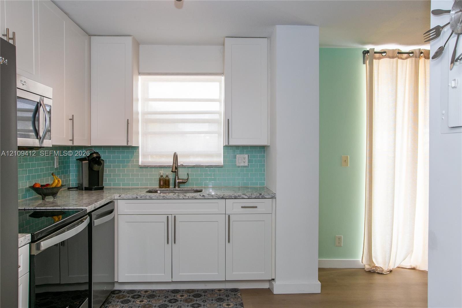 Kitchen featuring white shaker-style cabinetry, light-toned stone-finish countertops, stainless steel appliances, and a blue subway tile backsplash