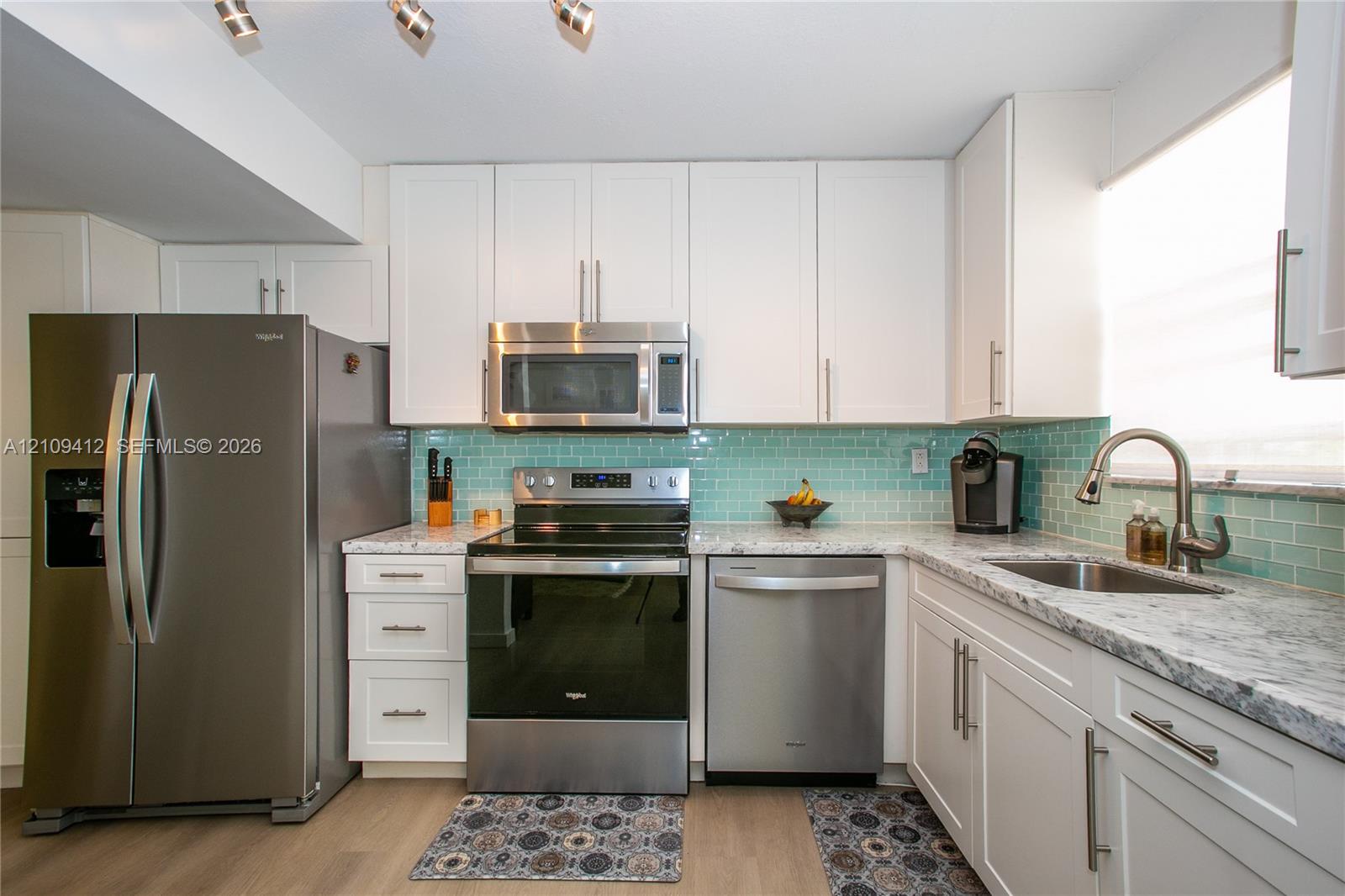 Kitchen featuring white shaker-style cabinetry, stainless steel appliances, speckled stone-finish countertops, a light blue glass subway tile backsplash, and wood-finish flooring