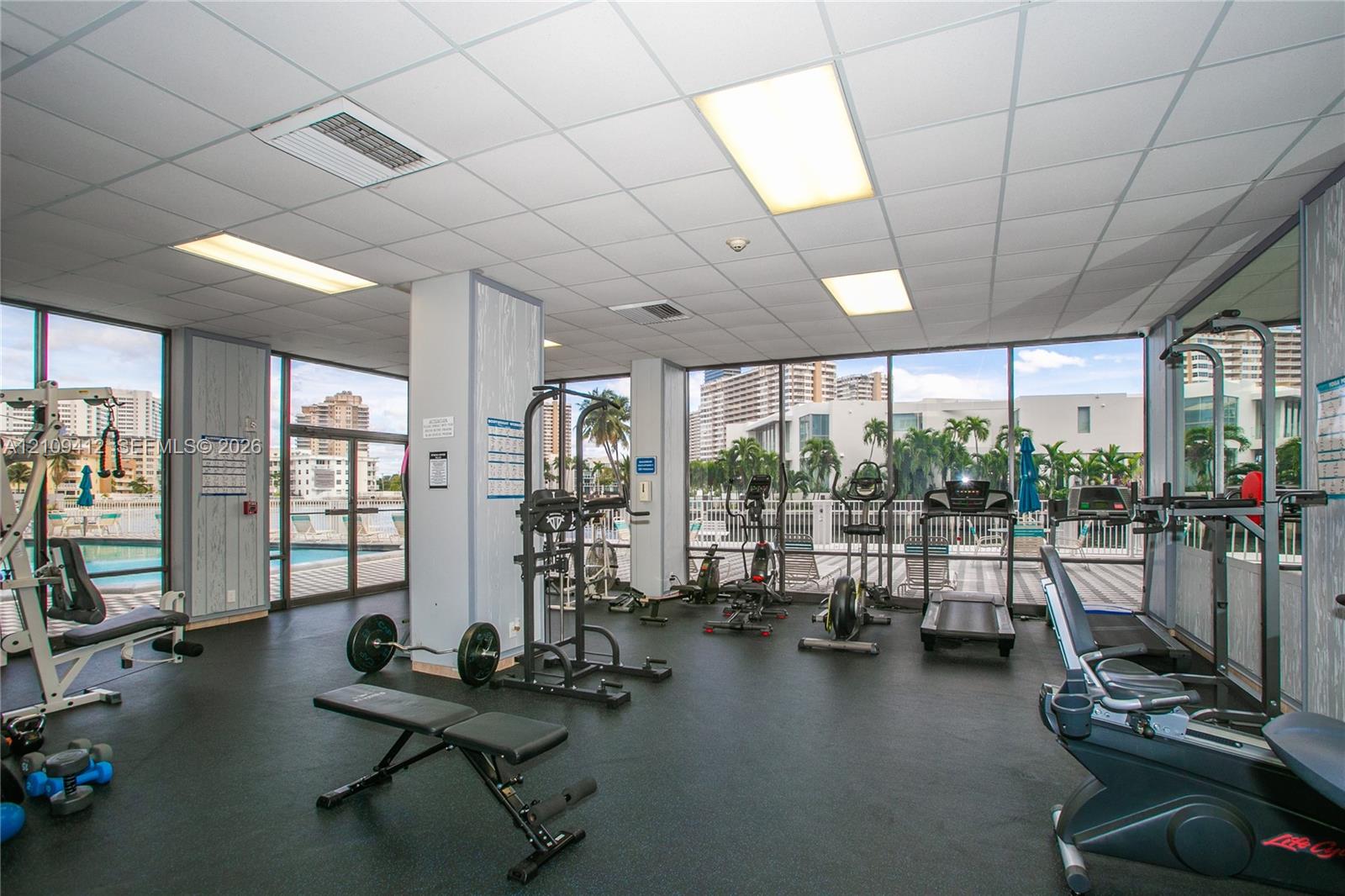 Fitness area featuring floor-to-ceiling windows, drop-tile ceiling with recessed lighting, and wall-to-wall rubberized flooring