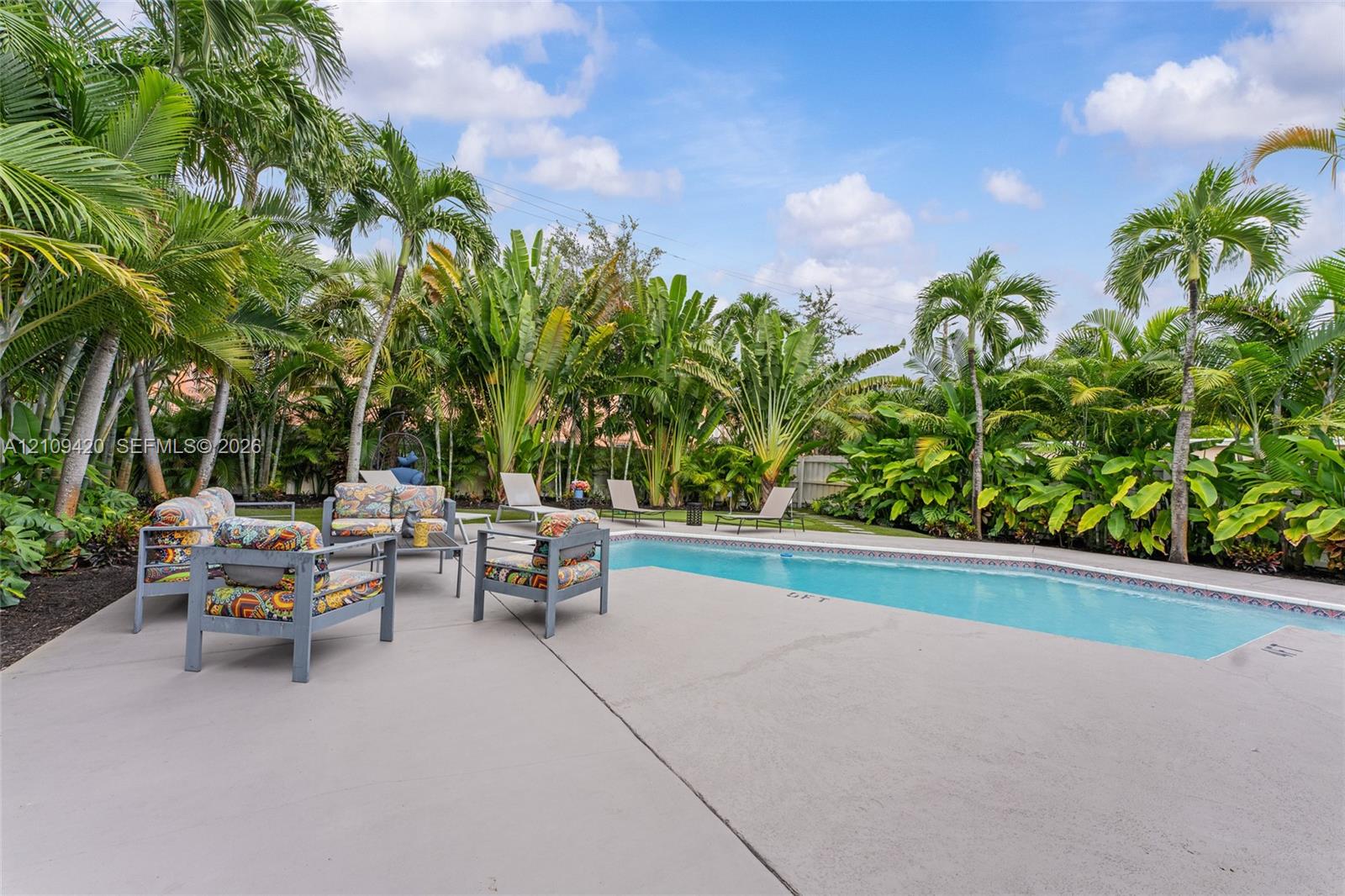 Backyard featuring a concrete pool deck, in-ground swimming pool, and dense tropical landscaping with mature palm trees