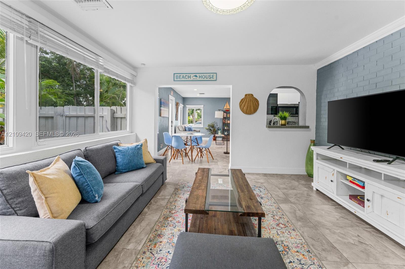 Living area featuring large windows, stone-finish tile flooring, a blue painted brick accent wall, and an arched passthrough opening