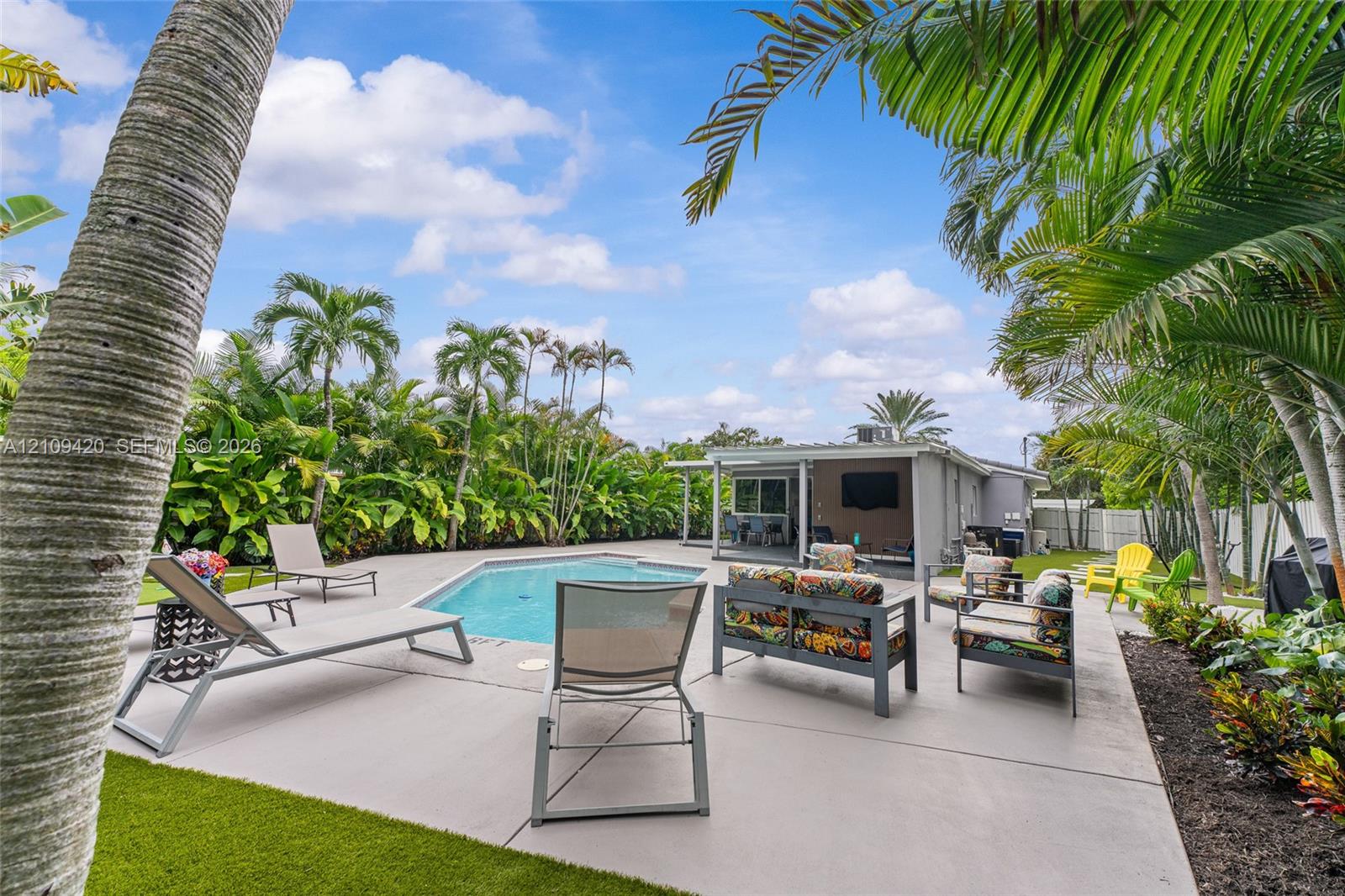 Outdoor living area featuring a swimming pool, concrete deck, covered patio, and established palm trees