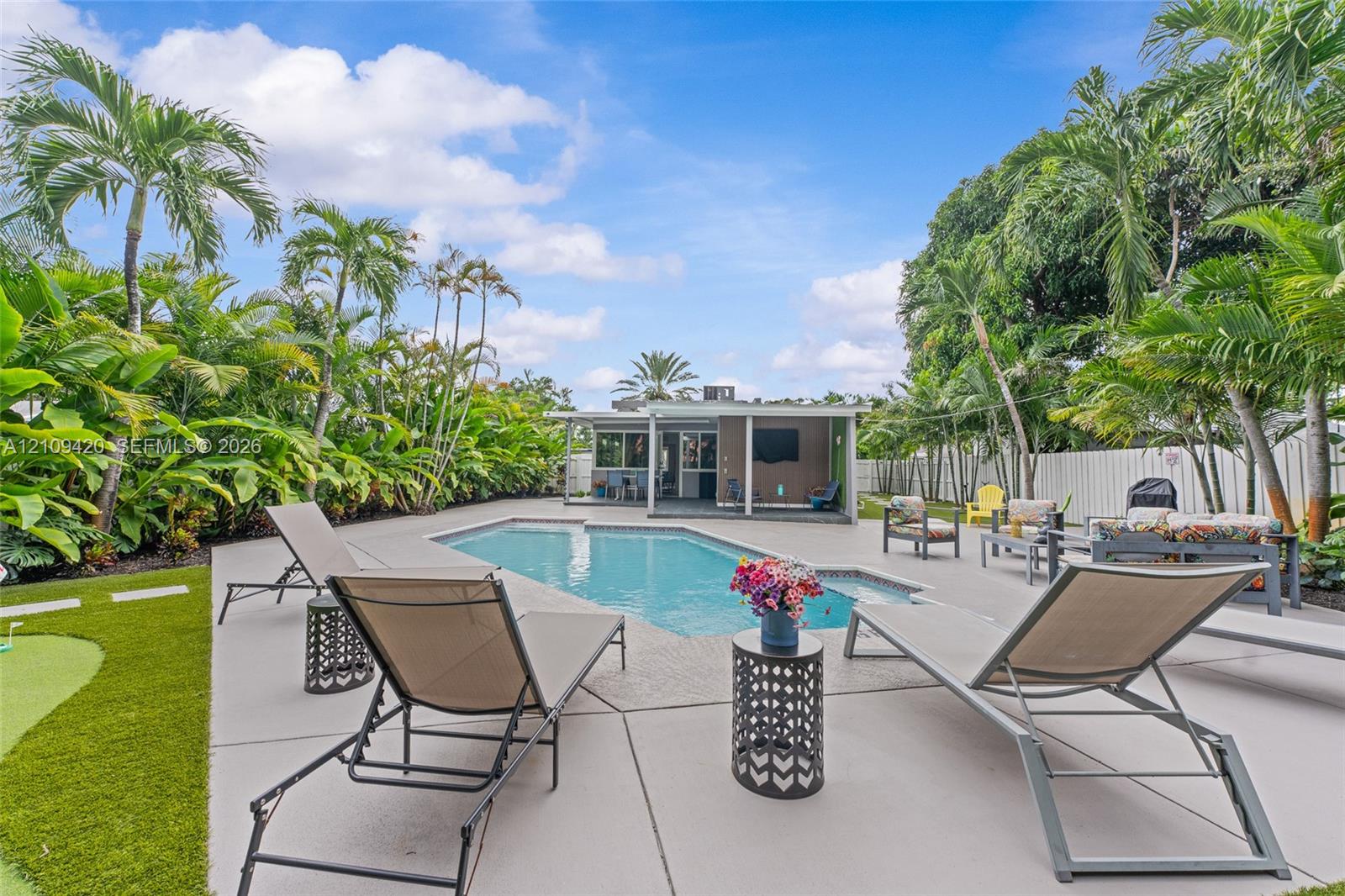 Private outdoor space featuring an in-ground swimming pool, concrete patio, artificial turf lawn, and mature palm tree landscaping