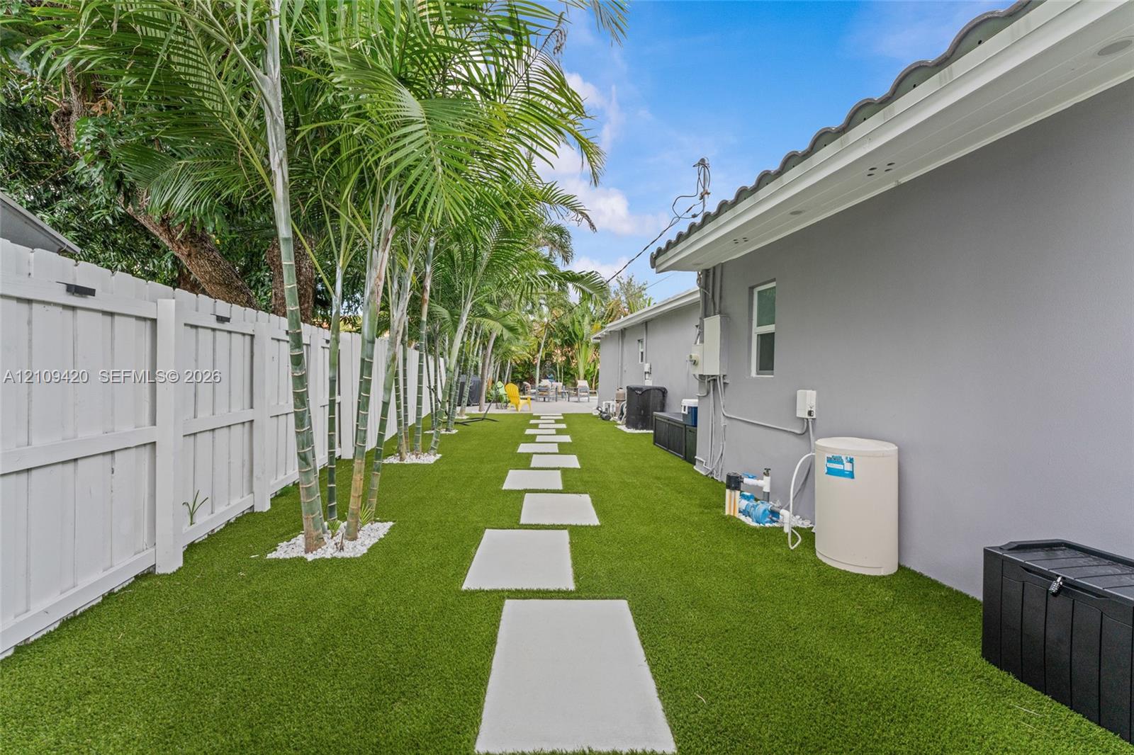 Side yard featuring synthetic turf, concrete paver pathway, privacy fencing, and mature palm trees