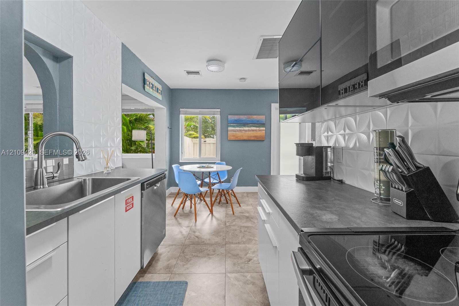 Kitchen featuring high-gloss black upper cabinetry, white lower cabinets, charcoal-toned countertops, three-dimensional geometric backsplash tile, and stainless-steel appliances