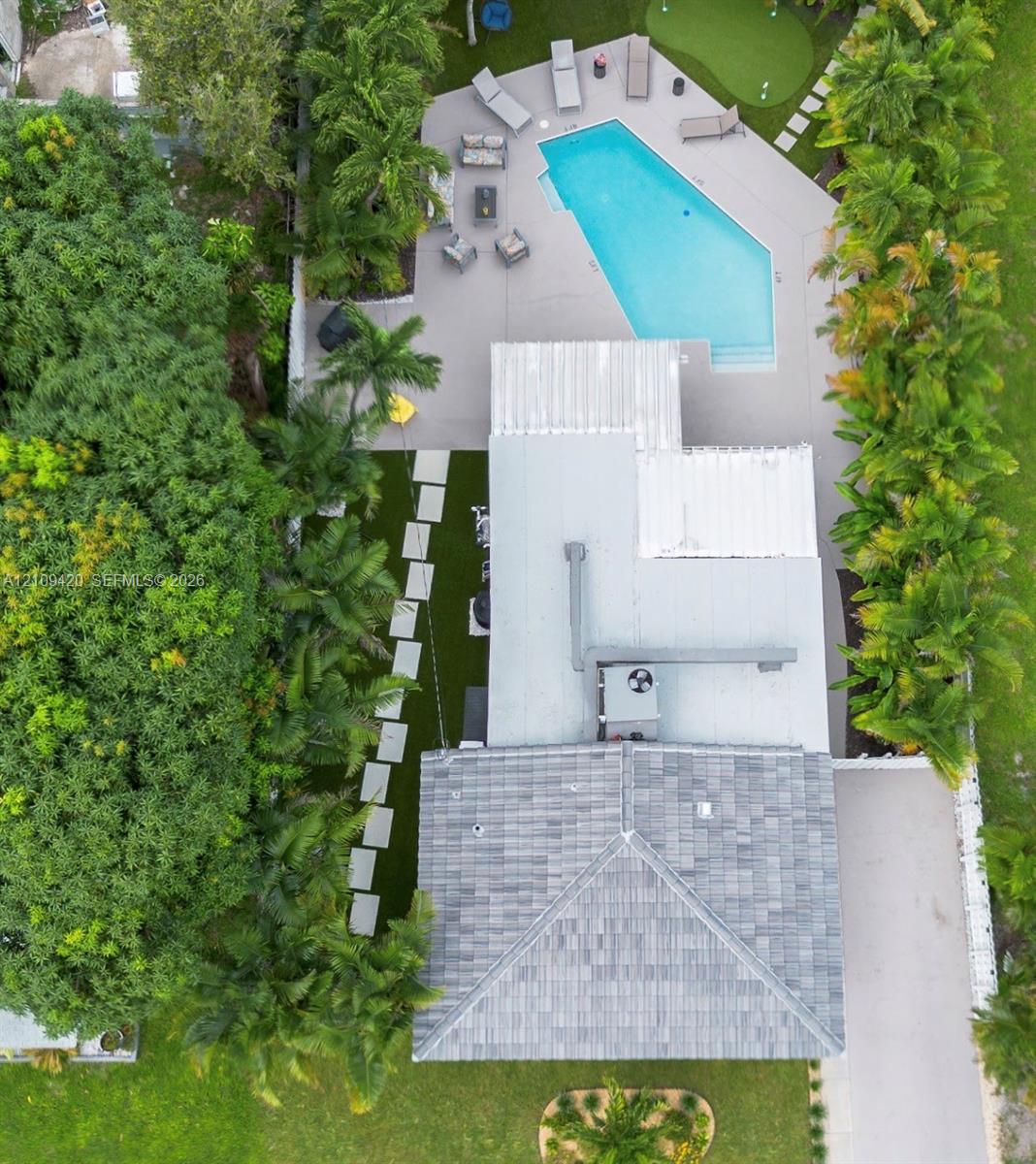 Aerial perspective of a rear yard featuring a pool, synthetic putting green, paved deck, and concrete paver walkway through a landscaped lawn