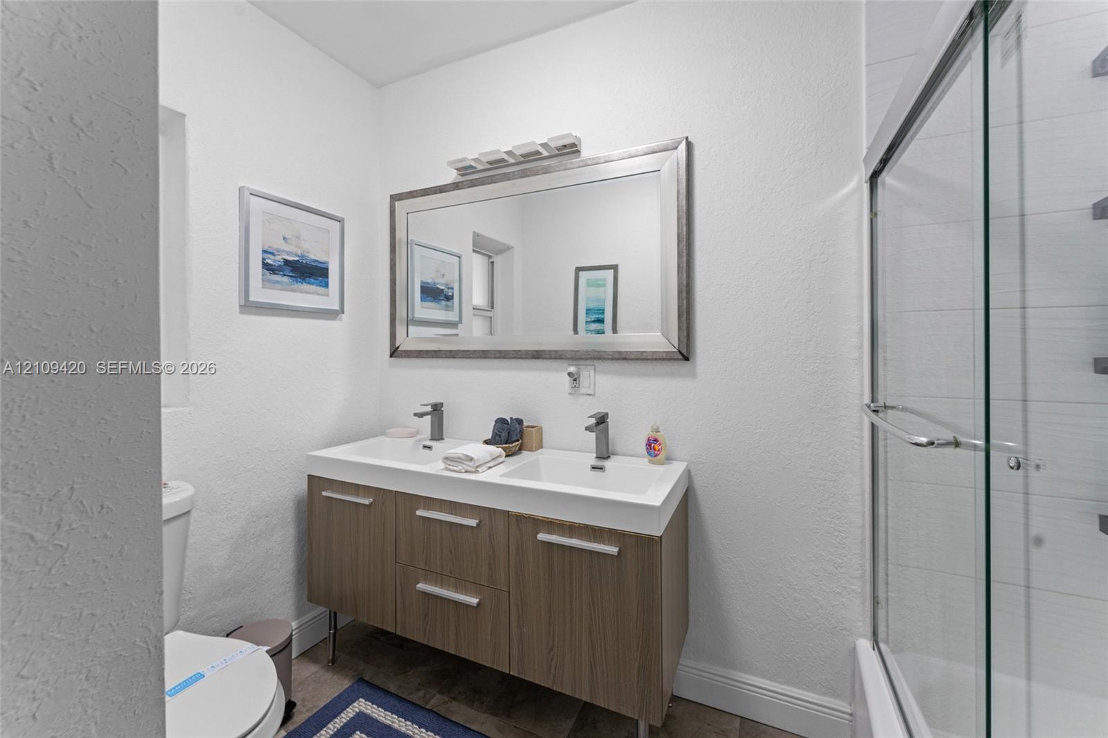 Floating vanity with a double-basin integrated countertop, metallic hardware, large rectangular wall mirror, and glass-enclosed shower