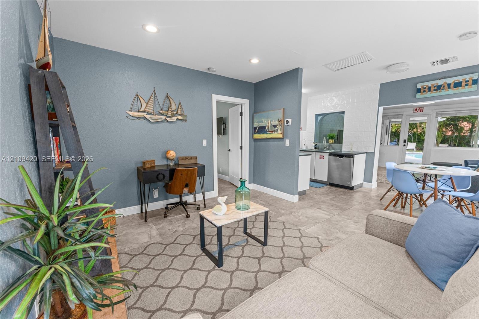 Living area featuring large-format tile flooring, recessed lighting, and a kitchen workspace with stainless steel appliances and crisp white cabinetry
