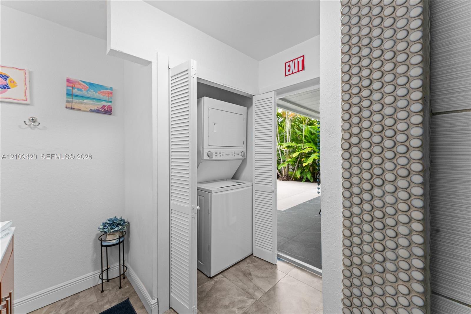 Laundry area featuring a stacked washer and dryer unit concealed behind bi-fold louvered doors, tile flooring, and a decorative circular mosaic tile accent wall