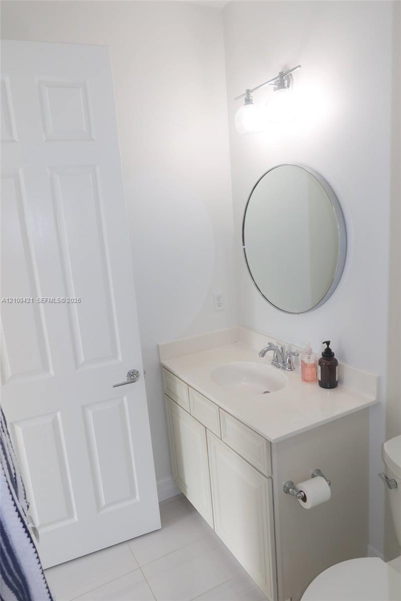 Bathroom featuring a vanity with a white solid-surface countertop, an integrated sink, polished chrome faucet, circular wall mirror, and dual-bulb vanity light