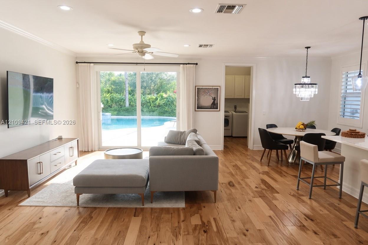 Open-concept living space featuring wood-finish flooring, recessed lighting, a ceiling fan, sliding glass doors, and a multi-tiered crystal pendant light