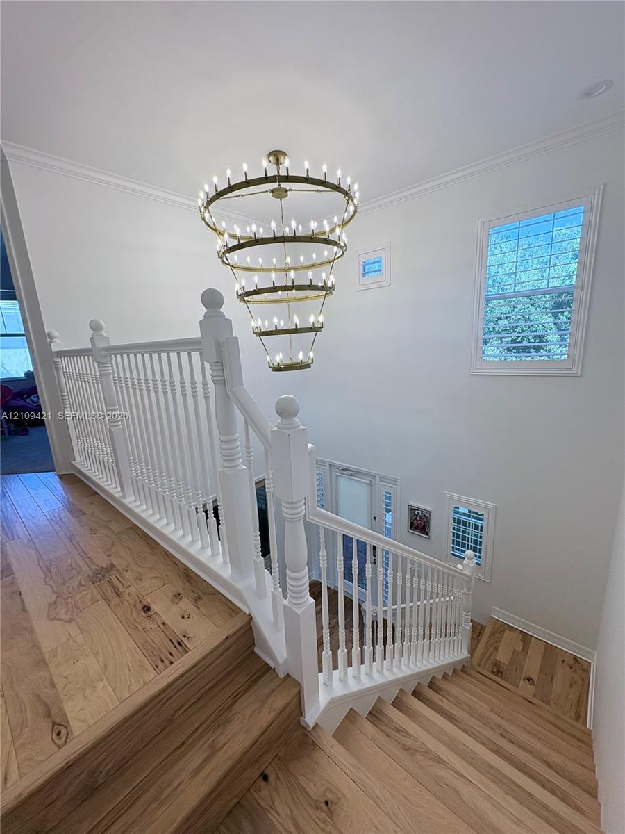 Multi-level staircase featuring wood-finish flooring, a white painted wood railing with detailed balusters, and a tiered brass candelabra chandelier
