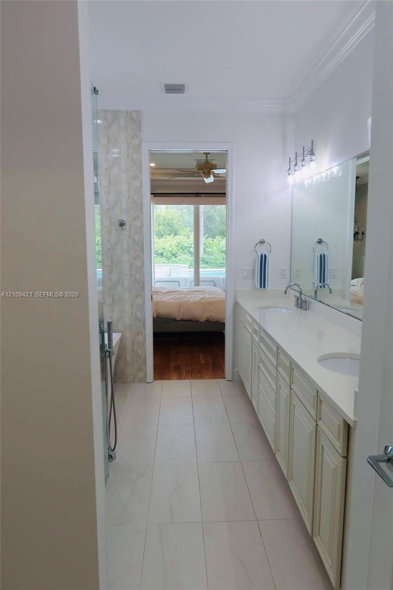 Bathroom featuring dual-sink vanity with light-tone cabinetry, quartz countertop, full-width wall mirror, and large-format tile flooring
