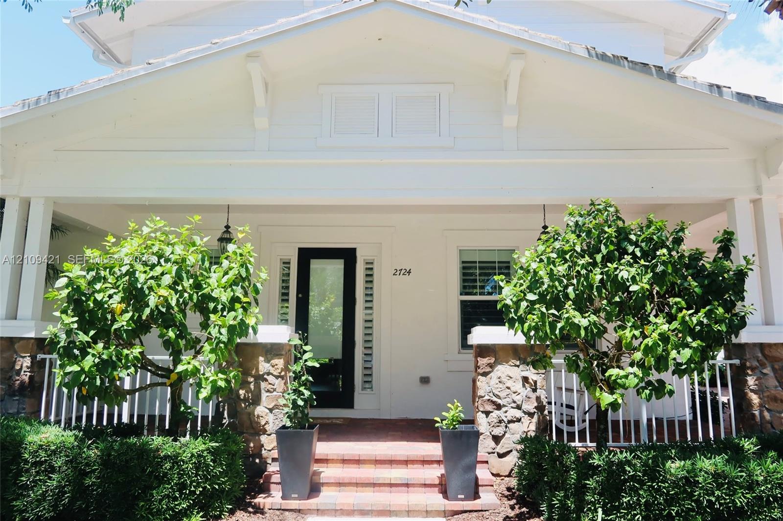 Covered front porch featuring a stone veneer base, white balustrades, brick-paver steps, and a glass-paneled entry door