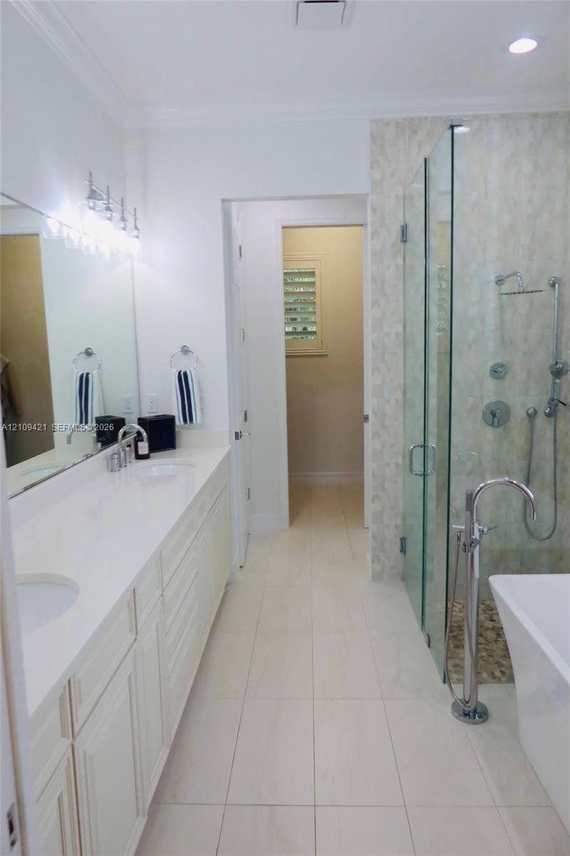 Dual-sink vanity with a solid-surface countertop, glass-enclosed walk-in shower with multi-head fixtures, freestanding soaking tub with floor-mounted faucet, and polished tile flooring