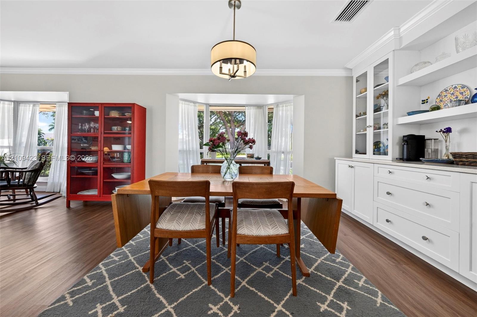 Dining space featuring wood-finish flooring, built-in cabinetry with glass-front display doors, open shelving, and a drum-style pendant light fixture