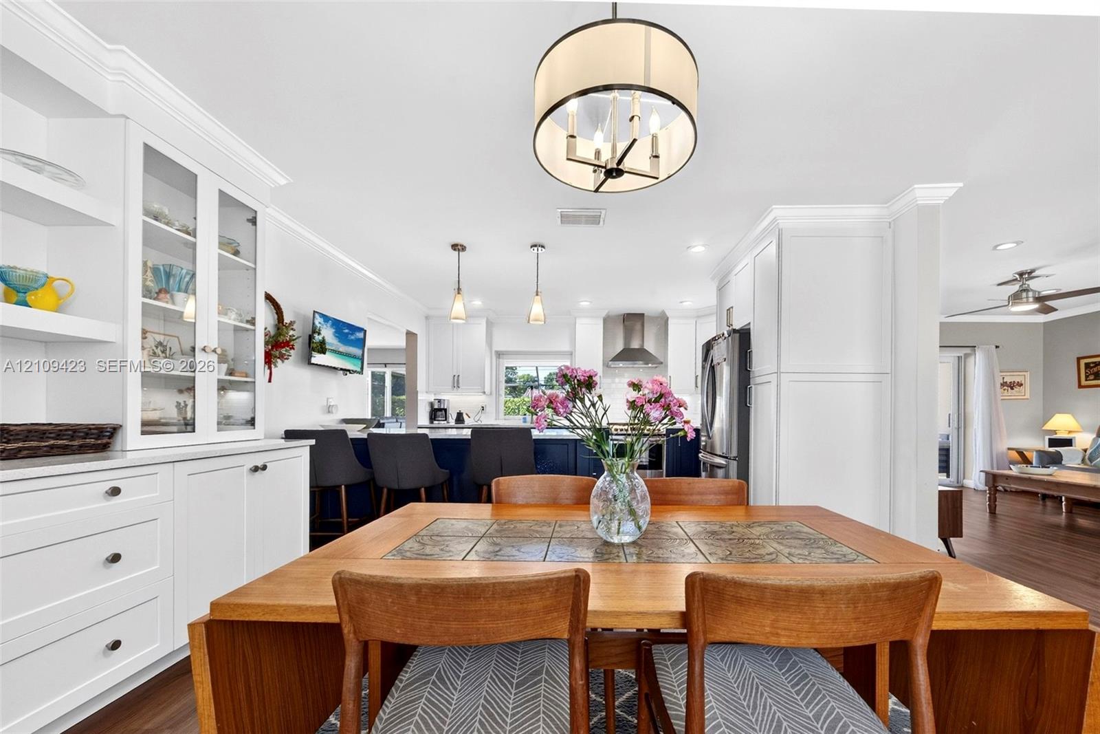 Built-in cabinetry with glass-front display shelving, recessed lighting, neutral crown molding, wood-finish flooring, and a decorative drum pendant light
