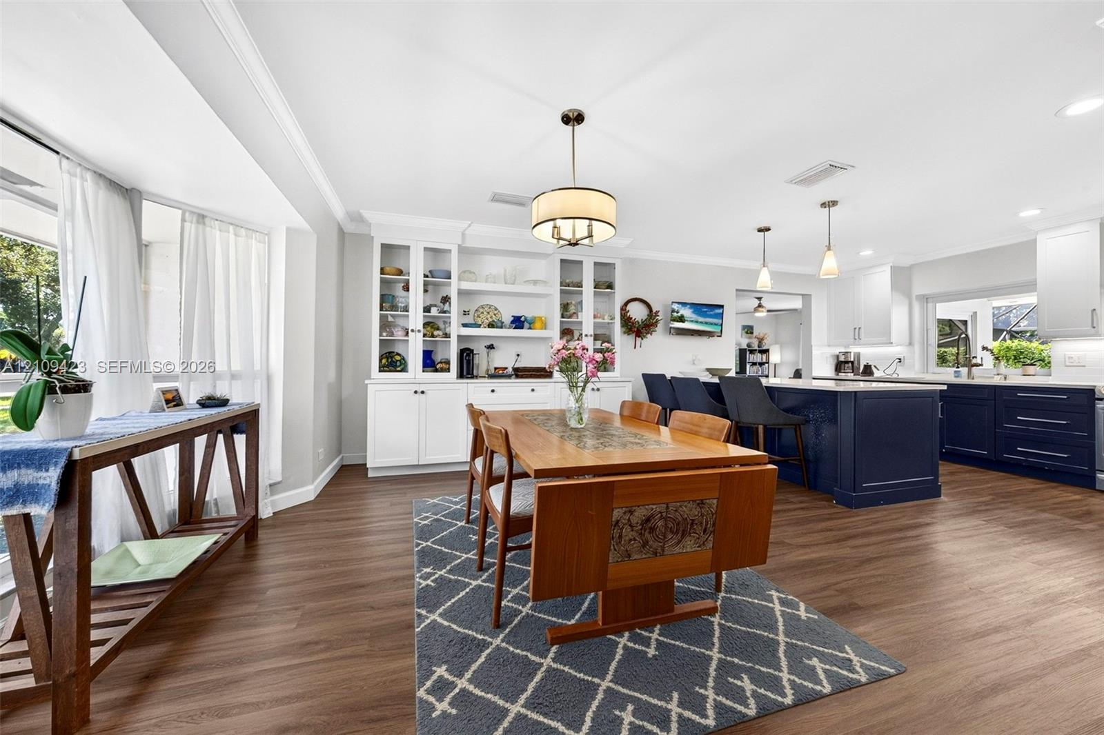 Kitchen featuring white upper cabinetry, a dark-toned center island, built-in display shelving, wood-finish flooring, and recessed lighting