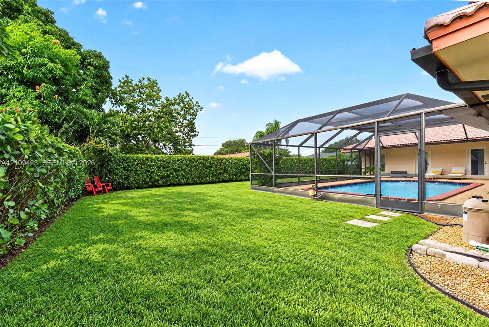 Expansive backyard featuring a screened-in swimming pool, manicured lawn, perimeter hedge, and stone paver path