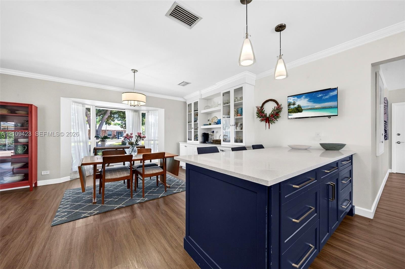Kitchen featuring a central island with a solid surface countertop, navy blue cabinetry, built-in display shelving, wood-finish flooring, and a bay window