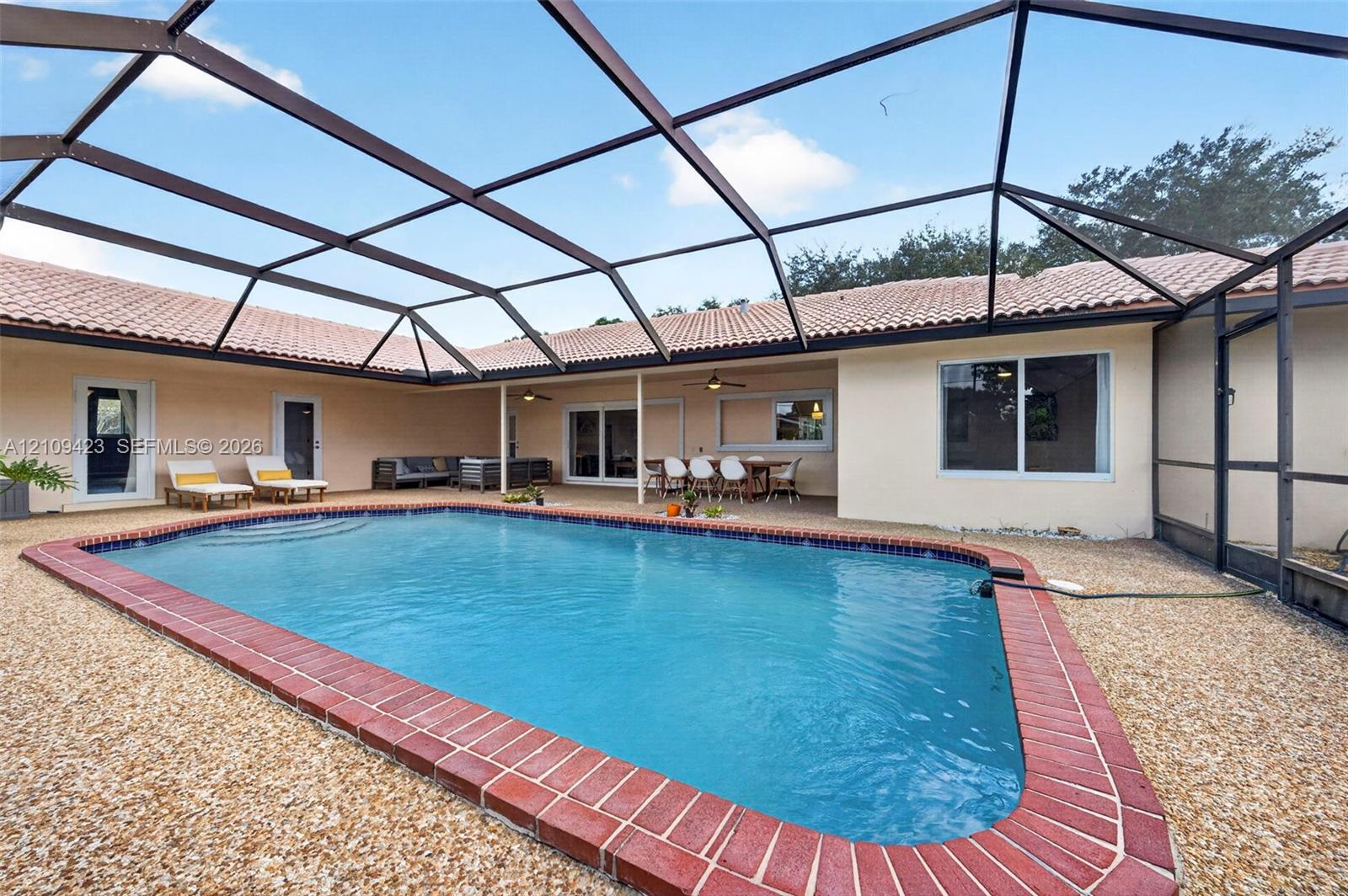 Screen-enclosed pool area featuring a tile-edged swimming pool, light-toned paved deck, and covered patio space with recessed lighting
