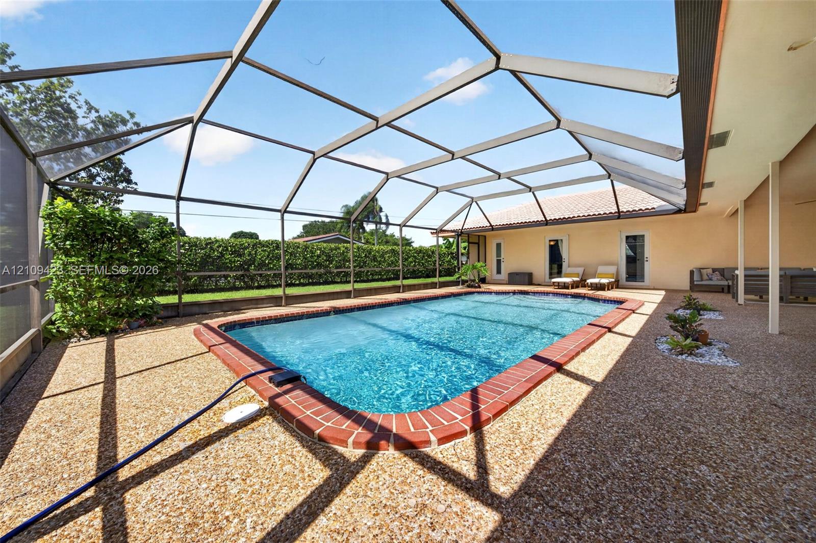 Screen-enclosed pool area with a brick-trimmed pool edge, textured aggregate patio surfacing, and a perimeter hedge